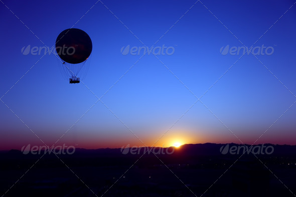 A hot air balloon silhouetted in the sky as the sun rises behind the desert mountains.