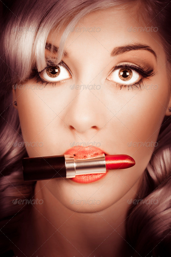 Pinup fashion portrait on the face of an attractive makeup artist woman holding red lipstick in between lips. Make-up and beauty products