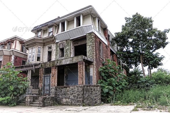 Vacant and abandoned empty boarded up house with overgrown vegetation in yard and derelict attached neighbor row home in a blight inner city urban neighborhood before rehabilitation and renewal