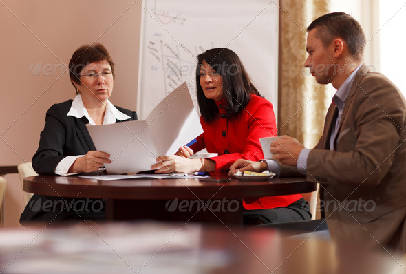 Businesspeople having a meeting over coffee sitting together at a table discussing a document, young man and two middle-aged women present