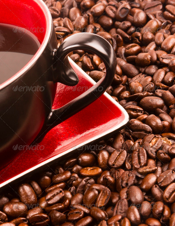 a flat pile group of roasted dark brown coffee beans with cup and saucer