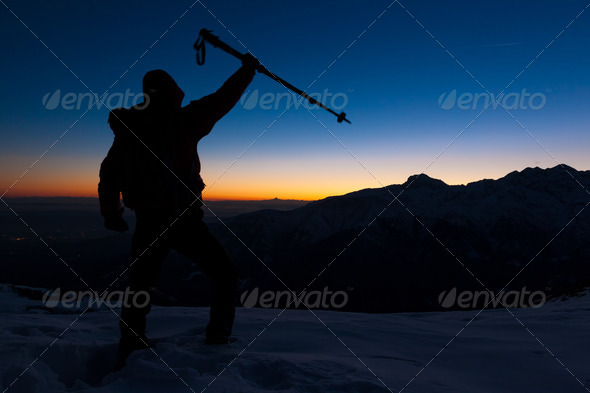 At sunset a man stands on a snowy peak expressing his joy for have reached the top of a mountain peak. Concept: adventure, achievement, sport.