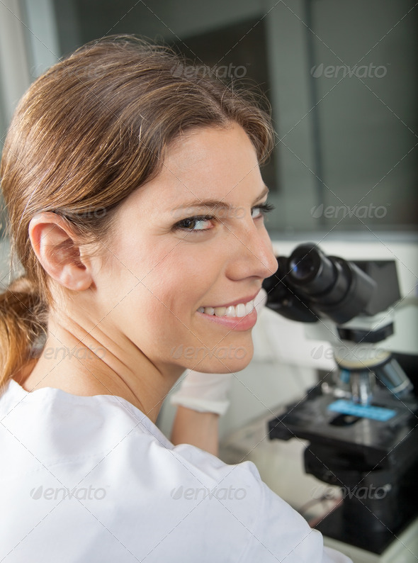 Portrait of happy young female scientist using microscope in laboratory