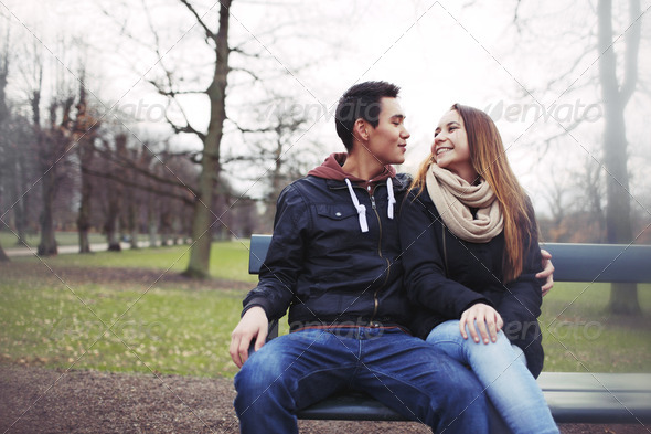 Happy young couple sitting on a bench outdoors during winter season. Asian teenage couple in warm clothes sitting on park bench.