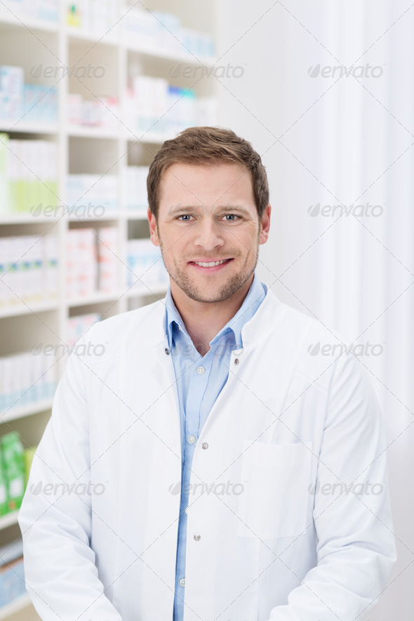 Smiling handsome male pharmacist standing in the pharmacy in his white coat