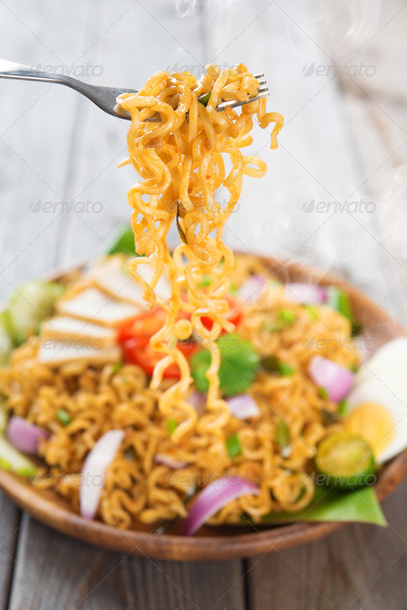 Spicy fried curry instant noodles or Malaysian style maggi goreng mamak. Ready to serve on wooden dining table setting. Fresh hot with steamed smoke.