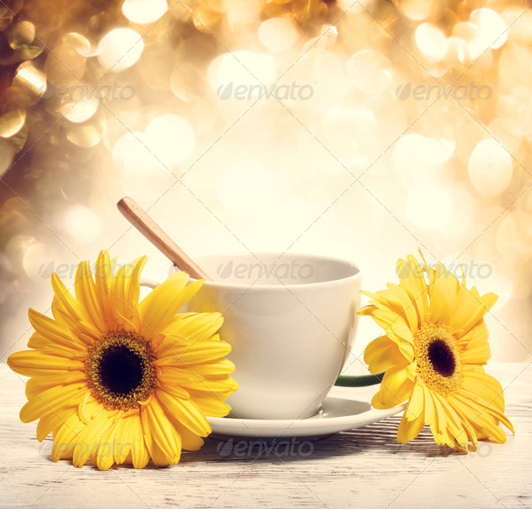 Coffee cup with yellow gerberas over shiny gold background