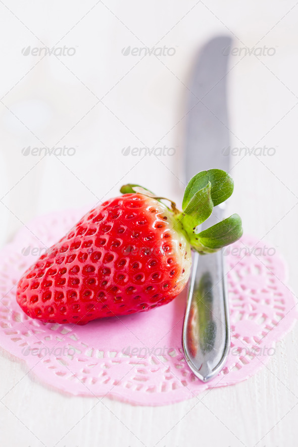 Closeup of fresh whole strawberry and silver metal knife resting on decorative pink mat