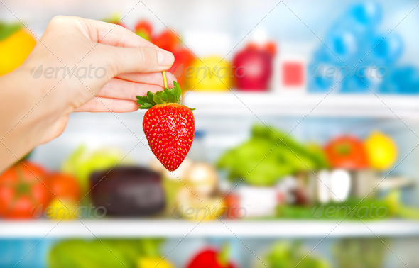 Eating healthy food conceptual background, weight loss and body care concept, fresh strawberry in hands, full fridge of diet nutrition, selective focus